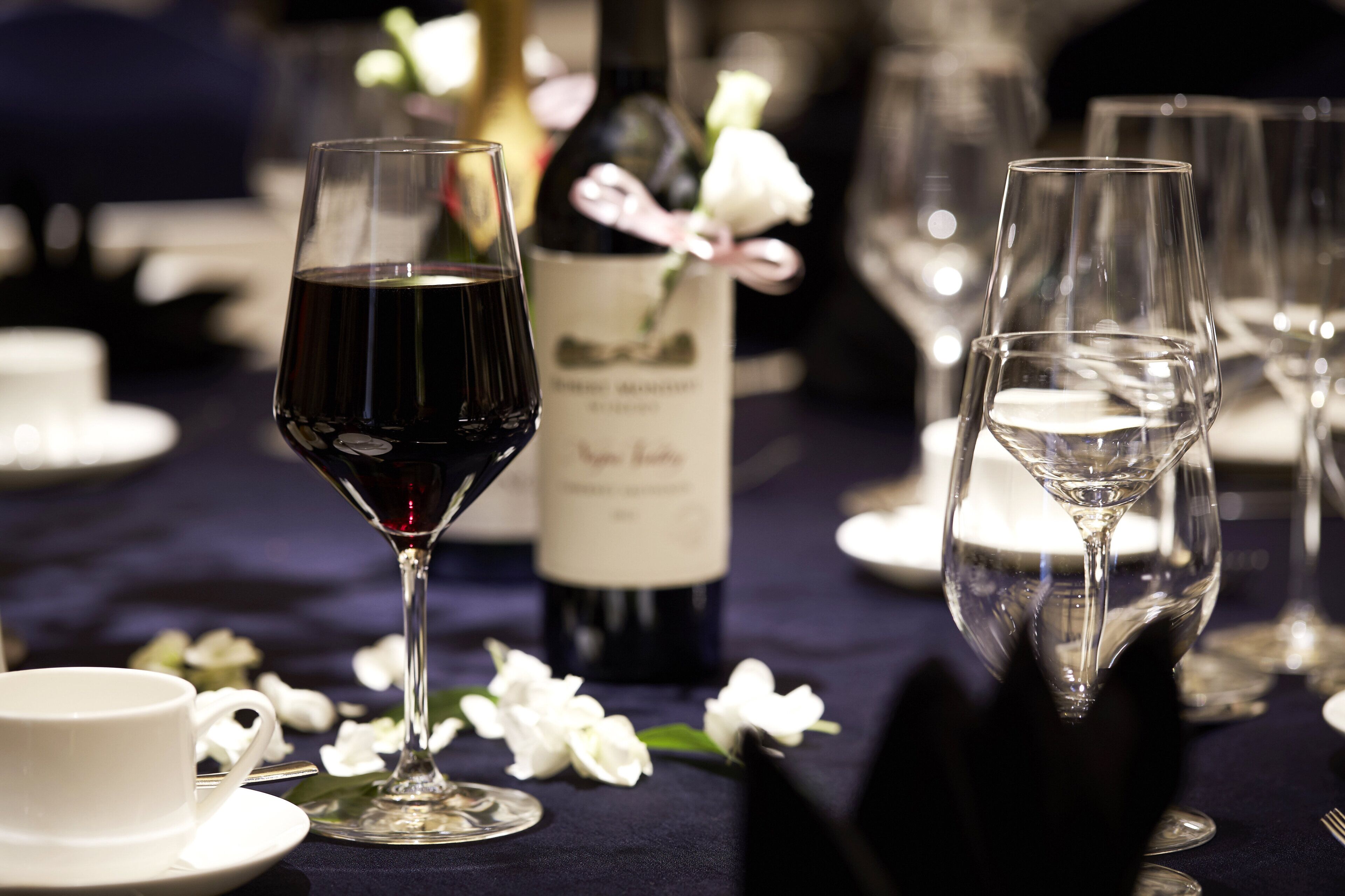 A table set for a meal with wine glasses, a bottle of wine, and a cup.