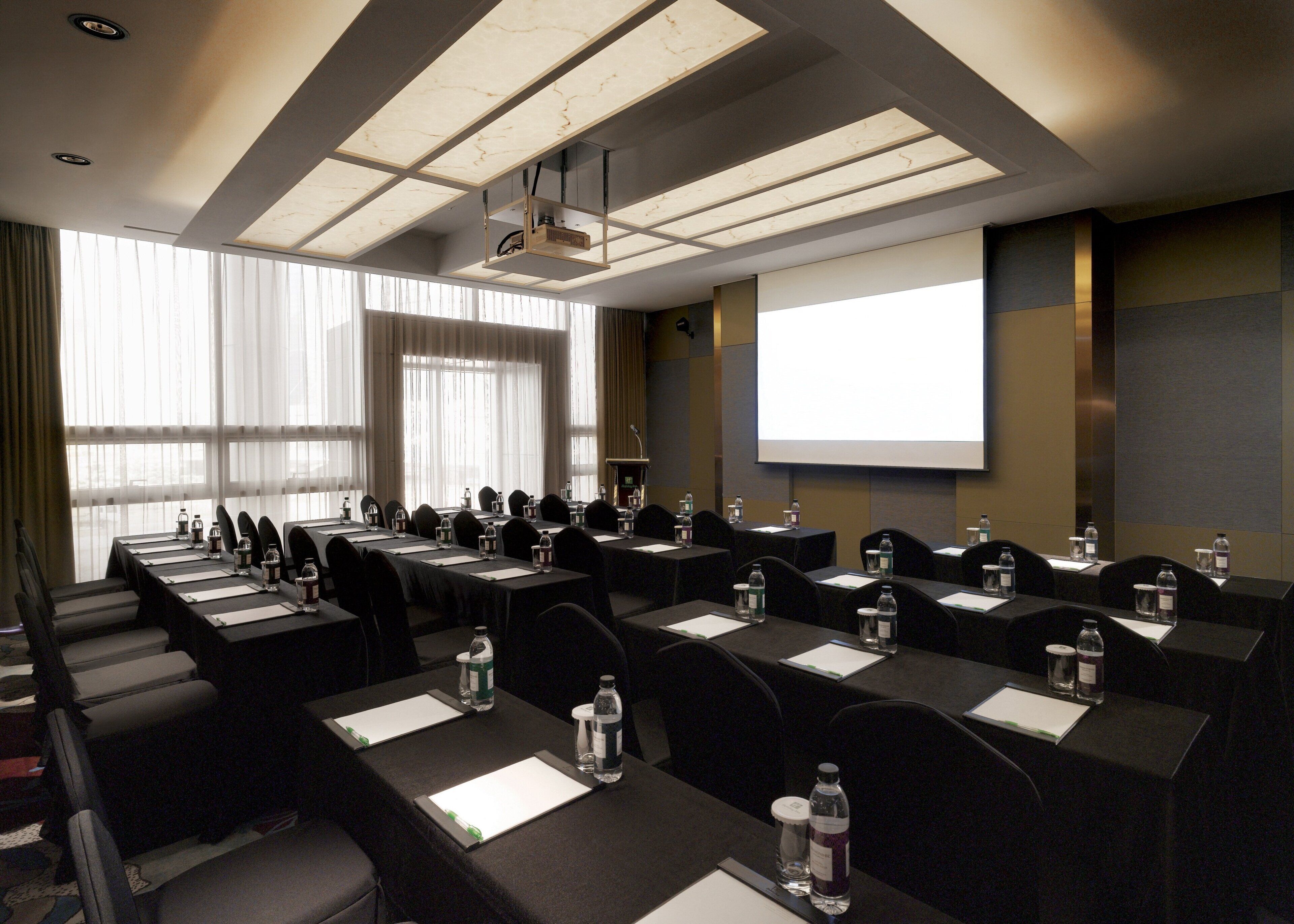 A conference room with multiple tables, chairs, and a projector screen.