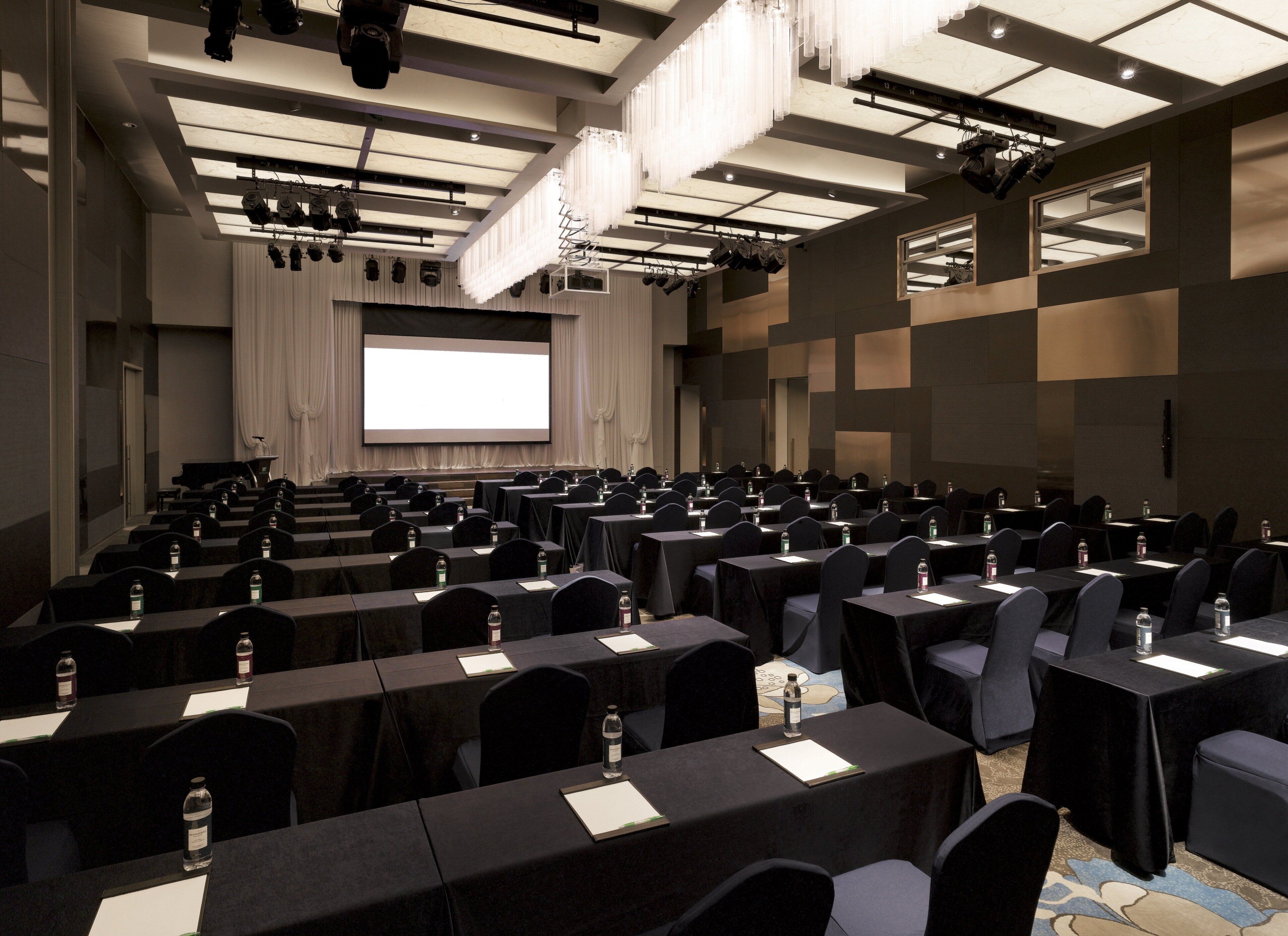 A conference room with rows of tables, chairs, and a large screen at the front.