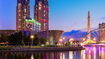 A cityscape with illuminated high-rise buildings, a bridge with a cable design, and a body of water reflecting the lights.