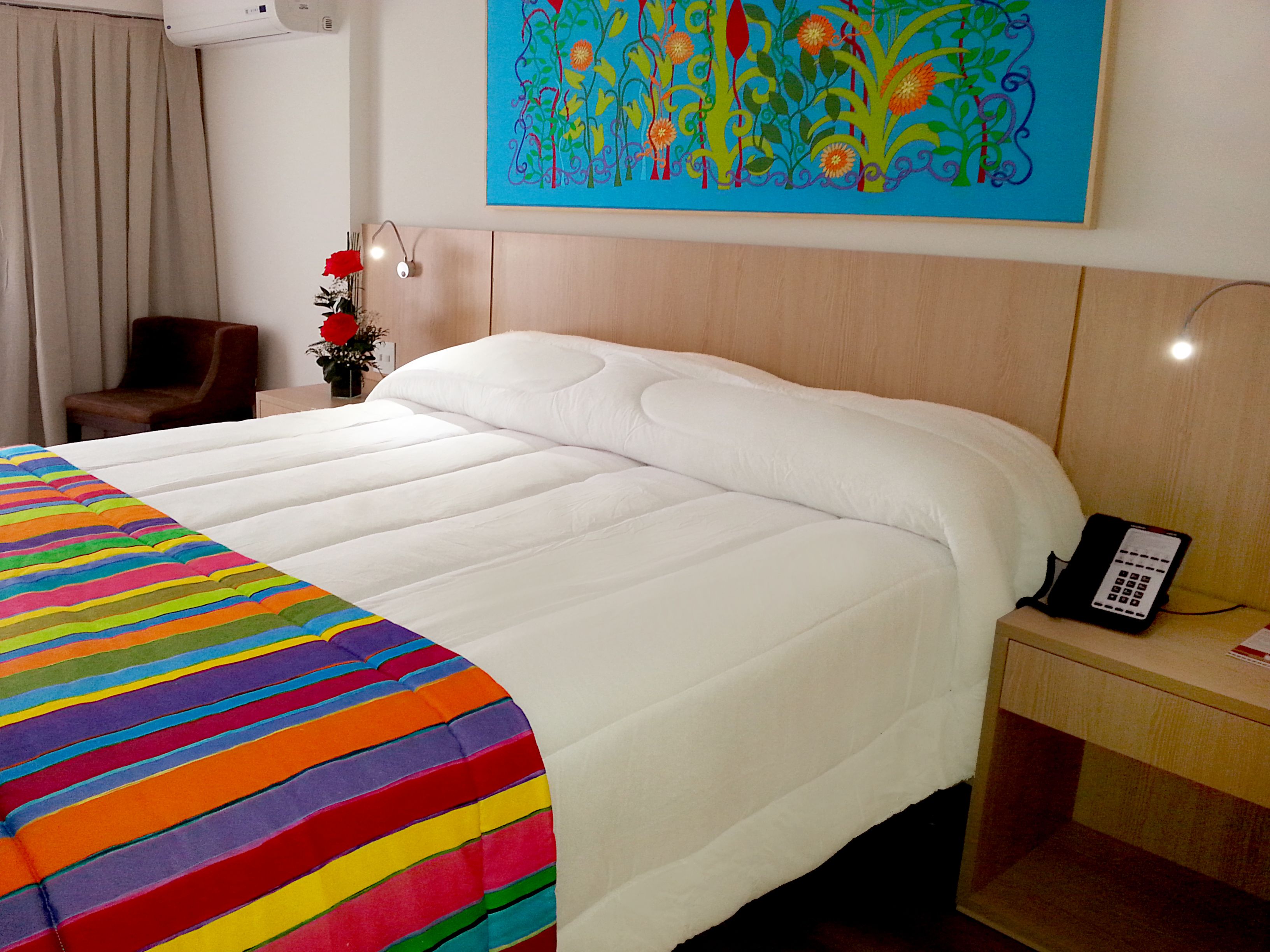 Une chambre d’hôtel avec un grand lit, une table de chevet avec un téléphone, une chaise et un tableau au mur.