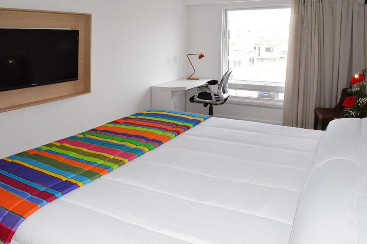 A hotel room with a bed, a desk, a chair, a TV, and a window with curtains.