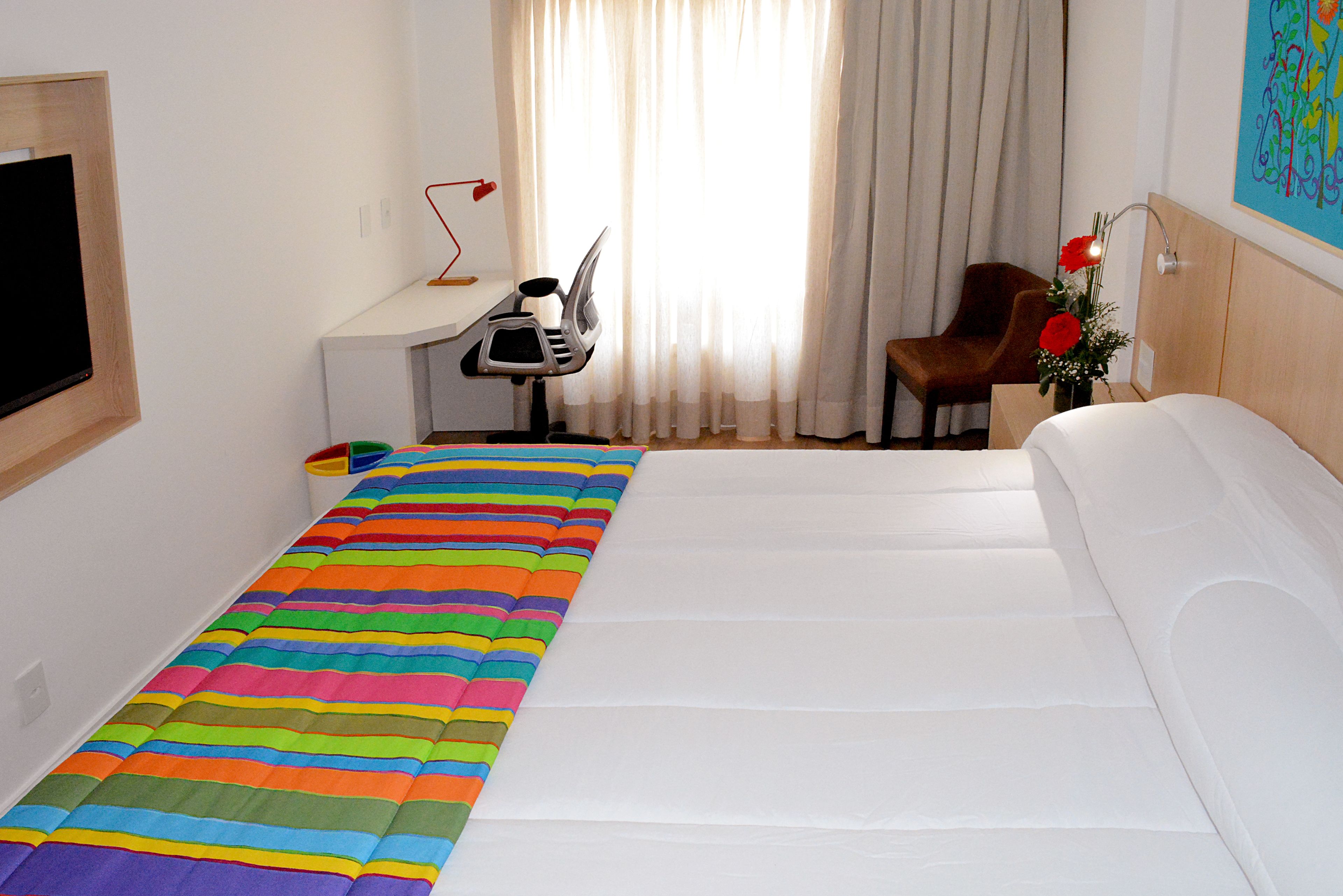 A hotel room with a bed, a desk with a chair, a TV, and a window with curtains.