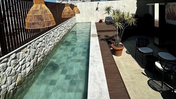 A pool area with a stone wall, lounge chairs, and a building with 'Eu Rio de Janeiro' signage. - Royalty Rio Hotel (Rio de Janeiro)