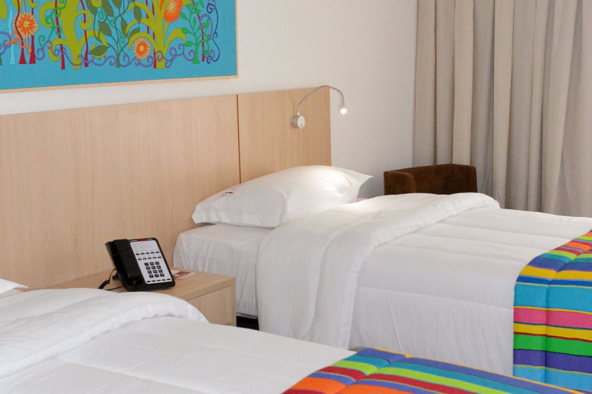 A hotel room with a large bed, a bedside table with a phone, a headboard, and a wall-mounted air conditioner.