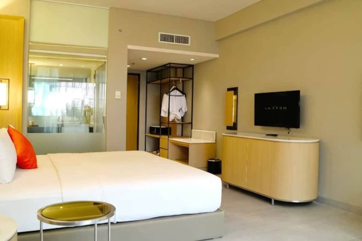 A hotel room with a bed, a TV, a small table, a mirror, and a wardrobe.