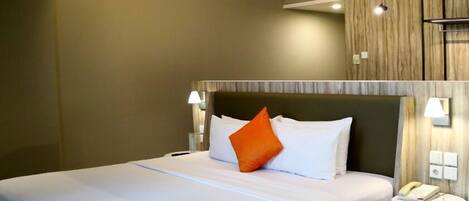 A hotel room with a bed, a bedside lamp, a round nightstand with a phone, and a wall-mounted air vent.