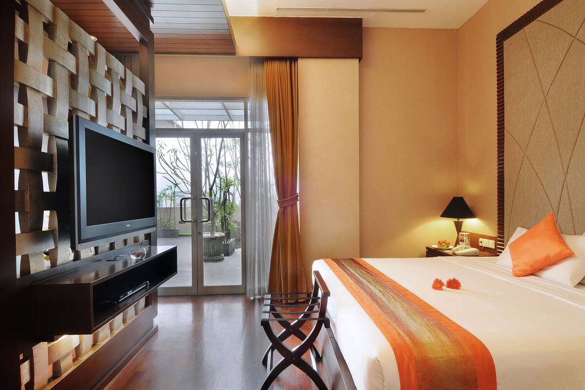 A hotel room with a bed, a TV, a desk, and a view of the outdoors.