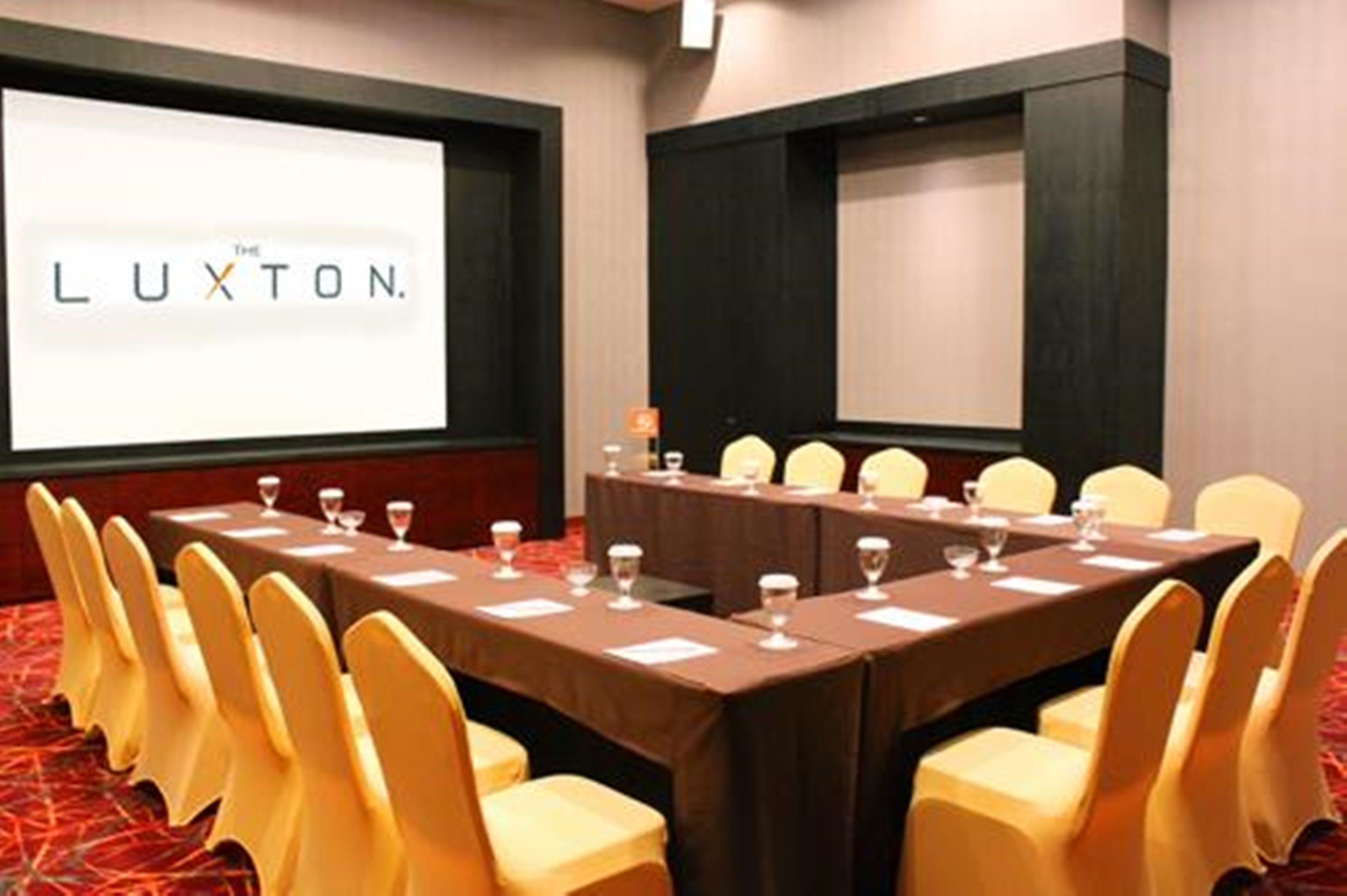 A conference room with a long table, yellow chairs, and a projector screen displaying "The Luxton."