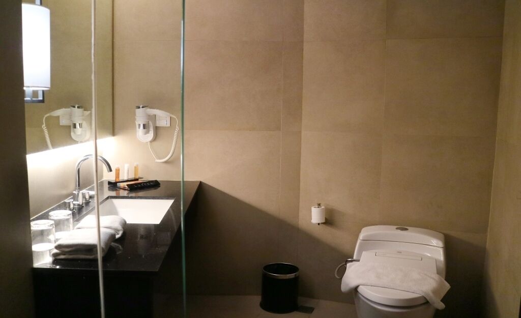 Un bagno moderno con un box doccia in vetro, un lavandino, un water e un cestino.