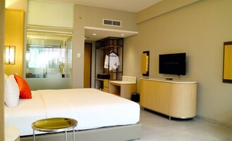 A modern hotel room with a large bed, a bedside table, a TV, a wardrobe, and a bathroom area.