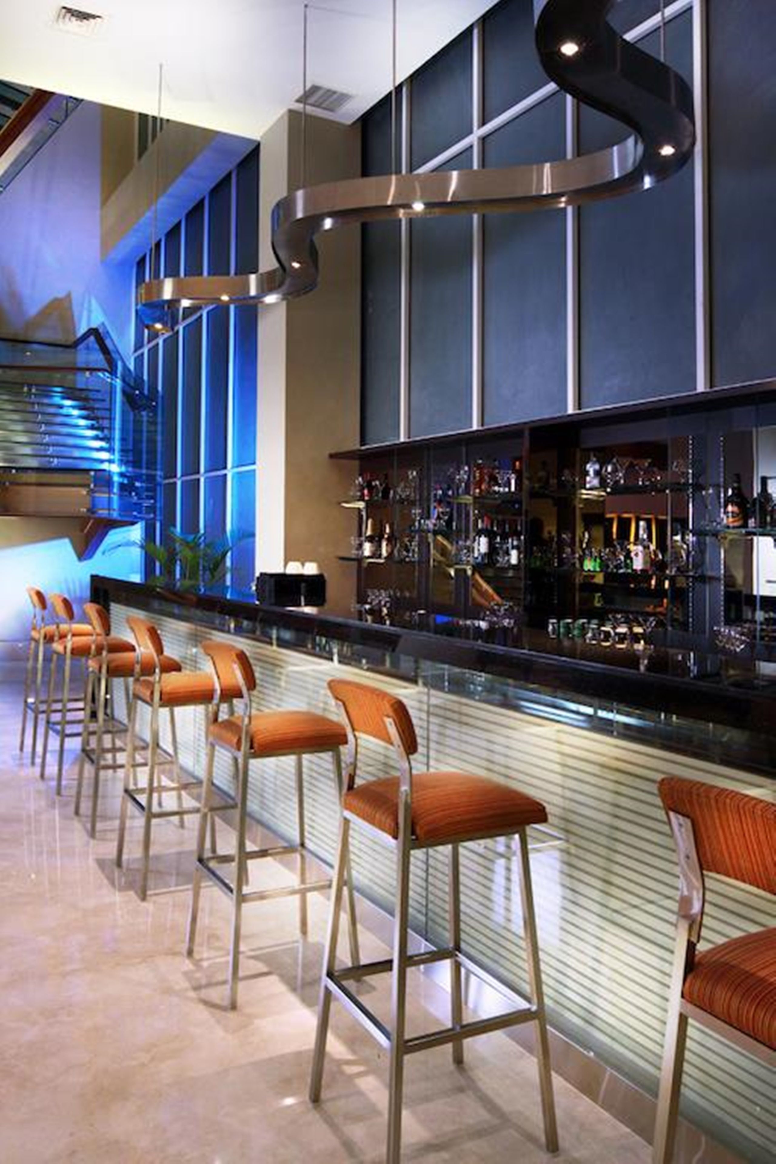 Una zona de bar con una barra alargada, varios taburetes y una variedad de botellas y vasos.