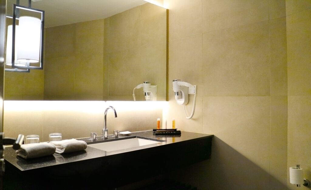 Un baño moderno con encimera negra, lavamanos, espejo, secador de pelo y toallero.