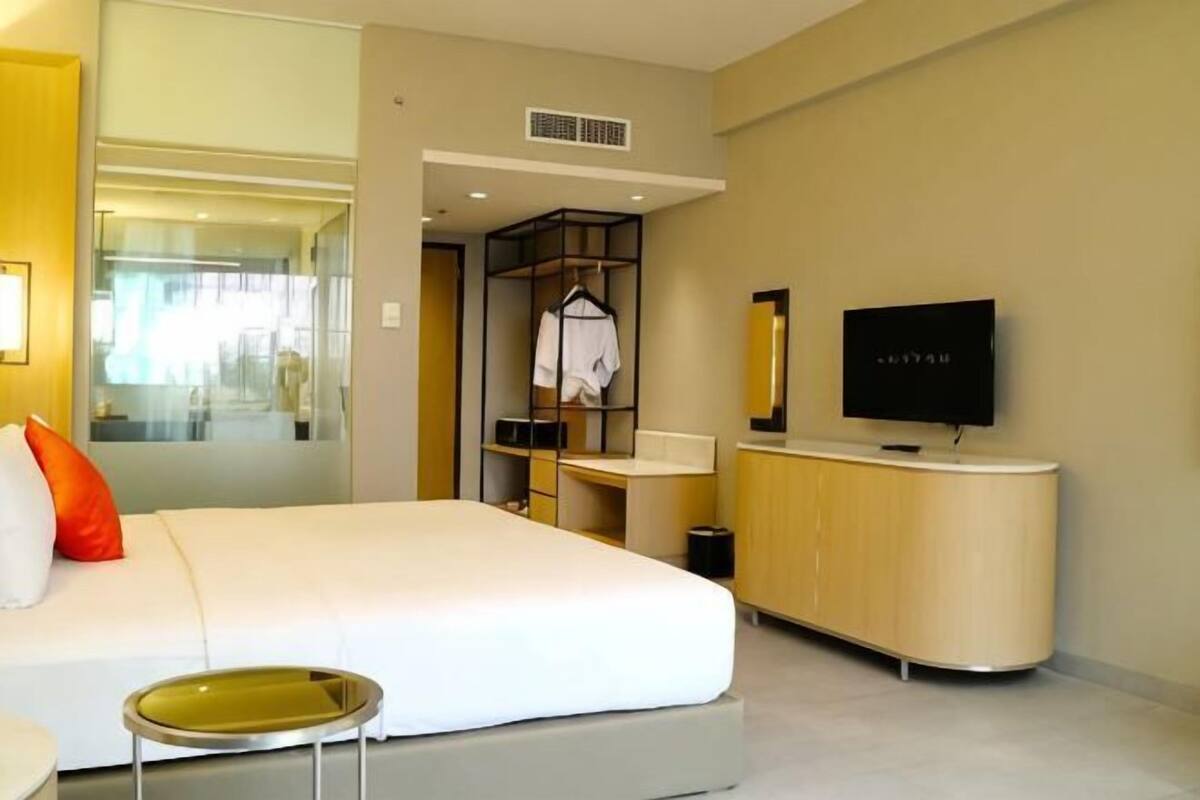 A hotel room with a bed, a TV, a small table, a mirror, and a wardrobe.