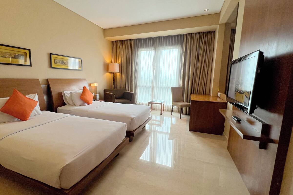 A hotel room with two beds, a TV, a desk, and a chair.