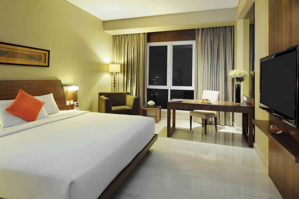 A hotel room with a bed, a desk, a chair, a television, and a window with curtains.