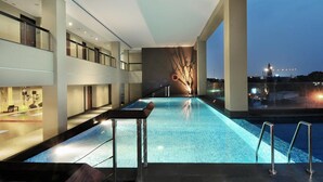 A modern indoor swimming pool with a view of the cityscape at dusk. - The Luxton Bandung (Bandung)