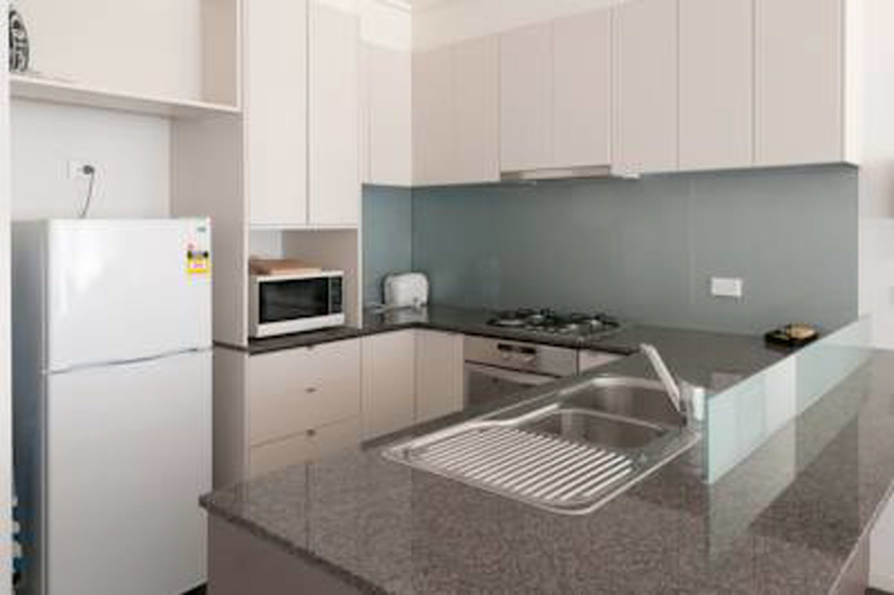 Une cuisine moderne avec des meubles blancs, un évier en acier inoxydable, un four à micro-ondes et une cuisinière à gaz.