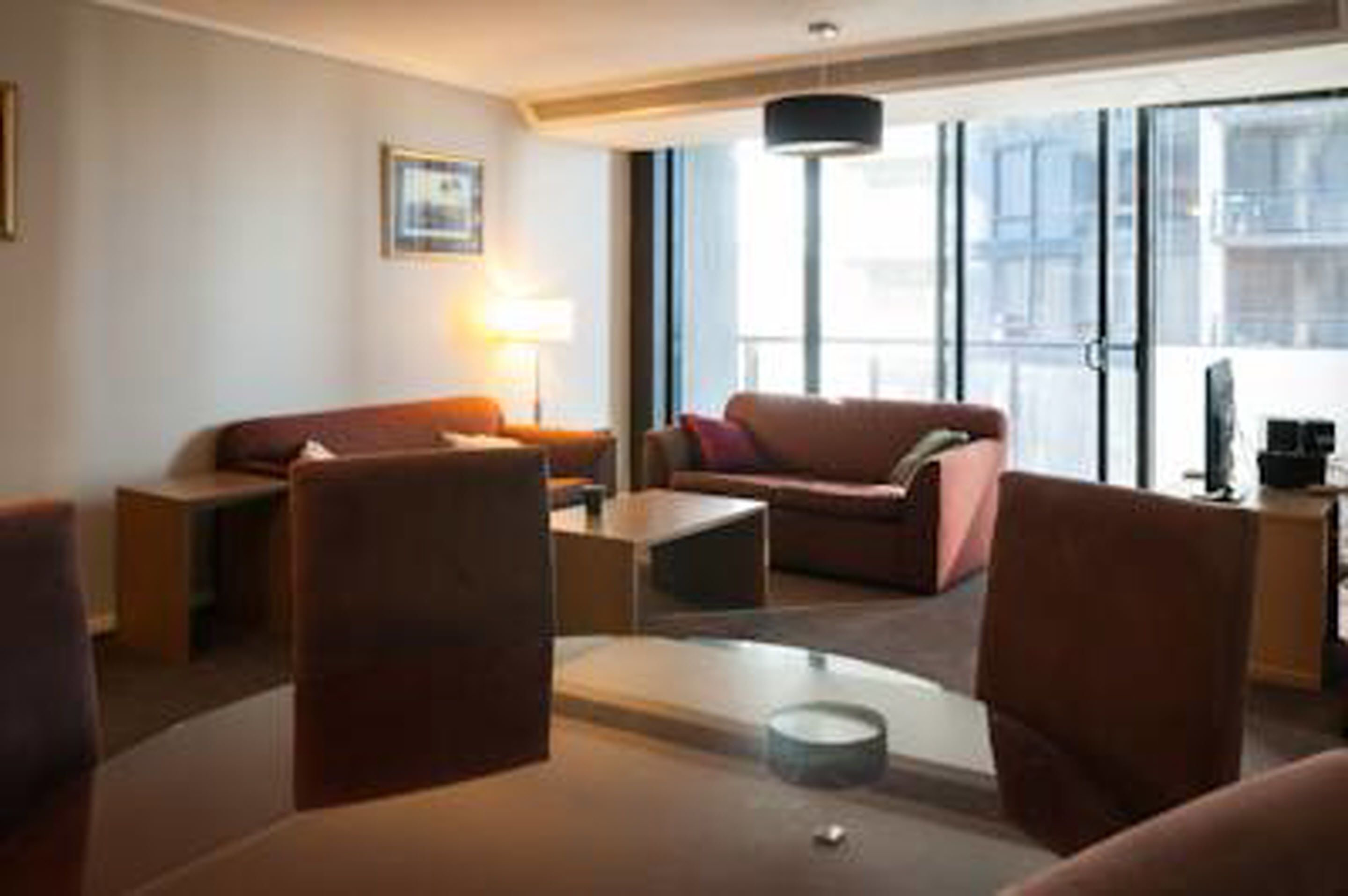 A modern hotel room with a sofa, armchairs, a coffee table, and a lamp.