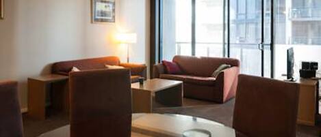 A modern hotel room with a sofa, armchairs, a coffee table, and a lamp.