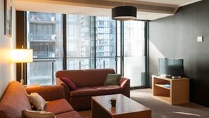 A modern living room with a sofa, coffee table, and a television on a stand. - Inner Melbourne Serviced Apartments (Southbank)