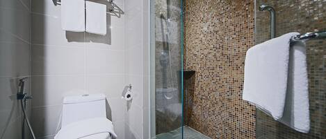 Un baño con inodoro, cabina de ducha de vidrio y pared de azulejos.