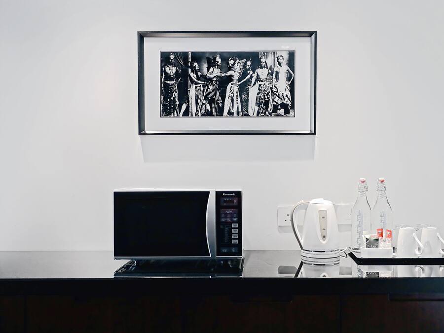 A framed black and white photograph on the wall, a Panasonic microwave, and a tray with coffee mugs and bottles.