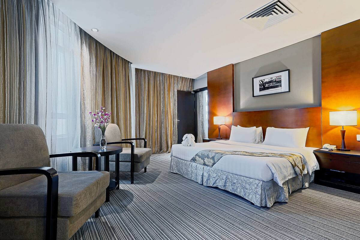 Una habitación de hotel con una cama grande, un escritorio, una silla y una mesita de noche con lámparas.