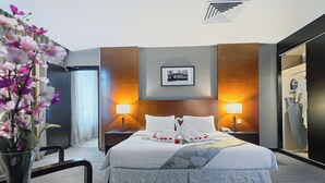 Una habitación de hotel con una cama grande, dos lámparas de noche, un cuadro en la pared y un jarrón con flores sobre la mesa.