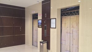 Un área de ascensor moderna con pared de paneles de madera, una pantalla informativa digital y un cubo de basura.