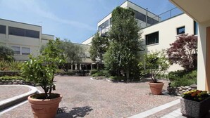 A courtyard with a paved walkway, potted plants, and a building with a balcony. - Venice Palace Hotel (Mirano)