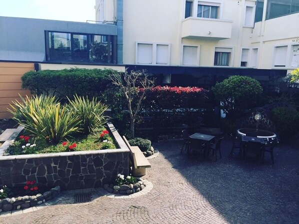 Un patio con una jardinera de piedra, mobiliario exterior y un edificio al fondo.