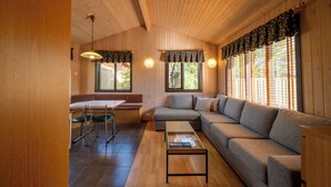 Een houten interieur met een bank, een eettafel met stoelen en een raam met jaloezieën.