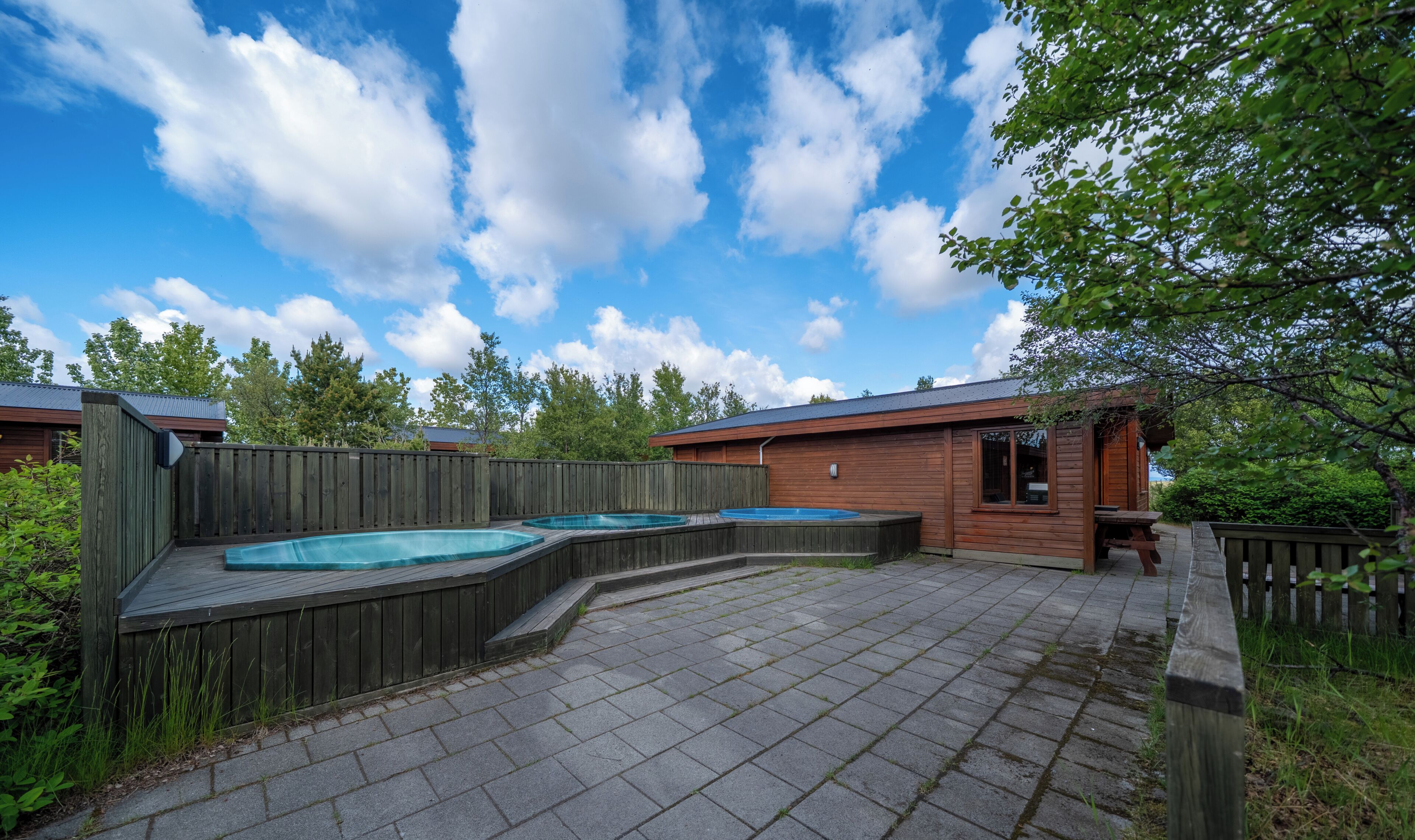 Un jardin avec une terrasse en bois, deux jacuzzis et un chalet en bois.