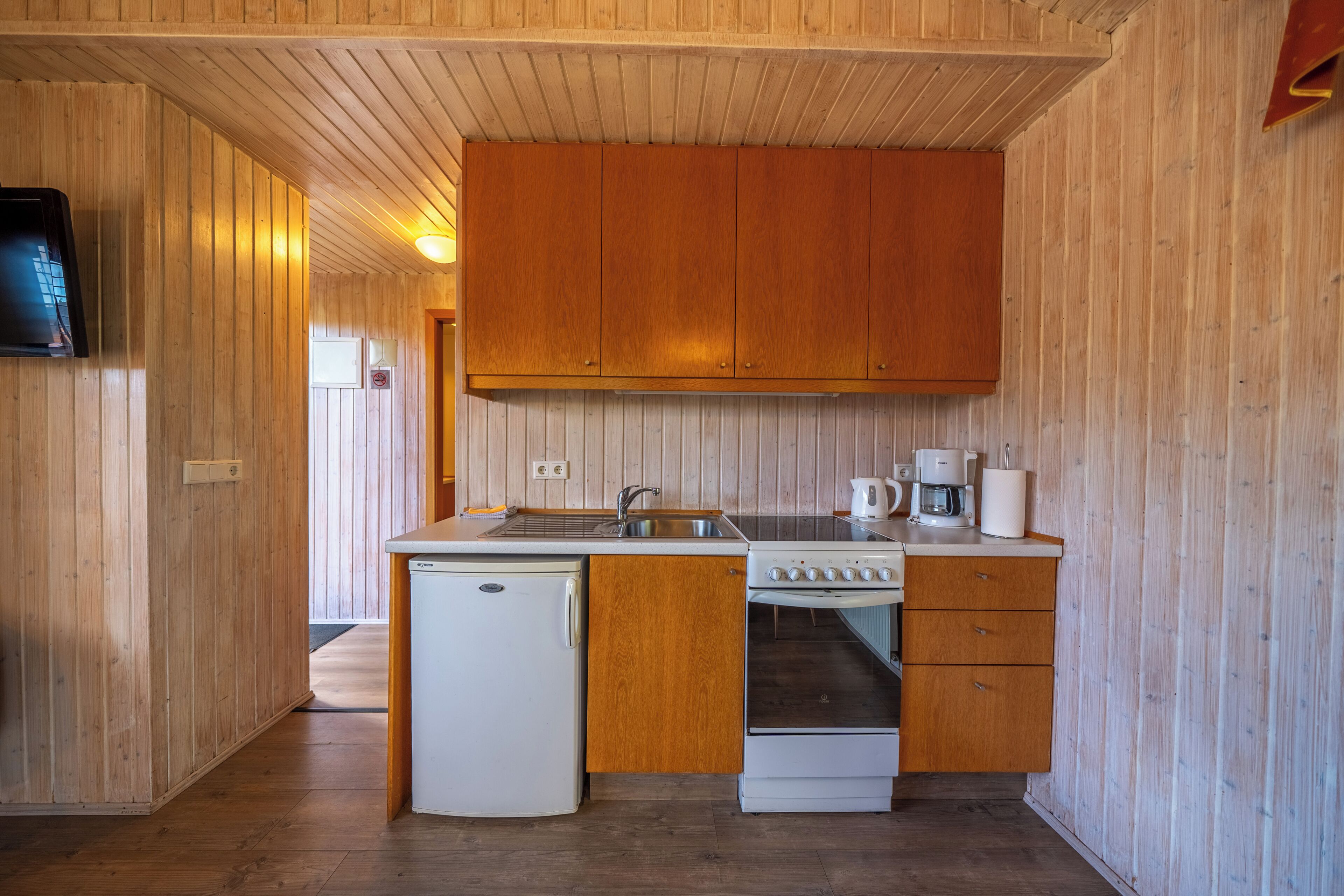 Een kleine keuken met houten kastjes, een koelkast, fornuis en gootsteen.