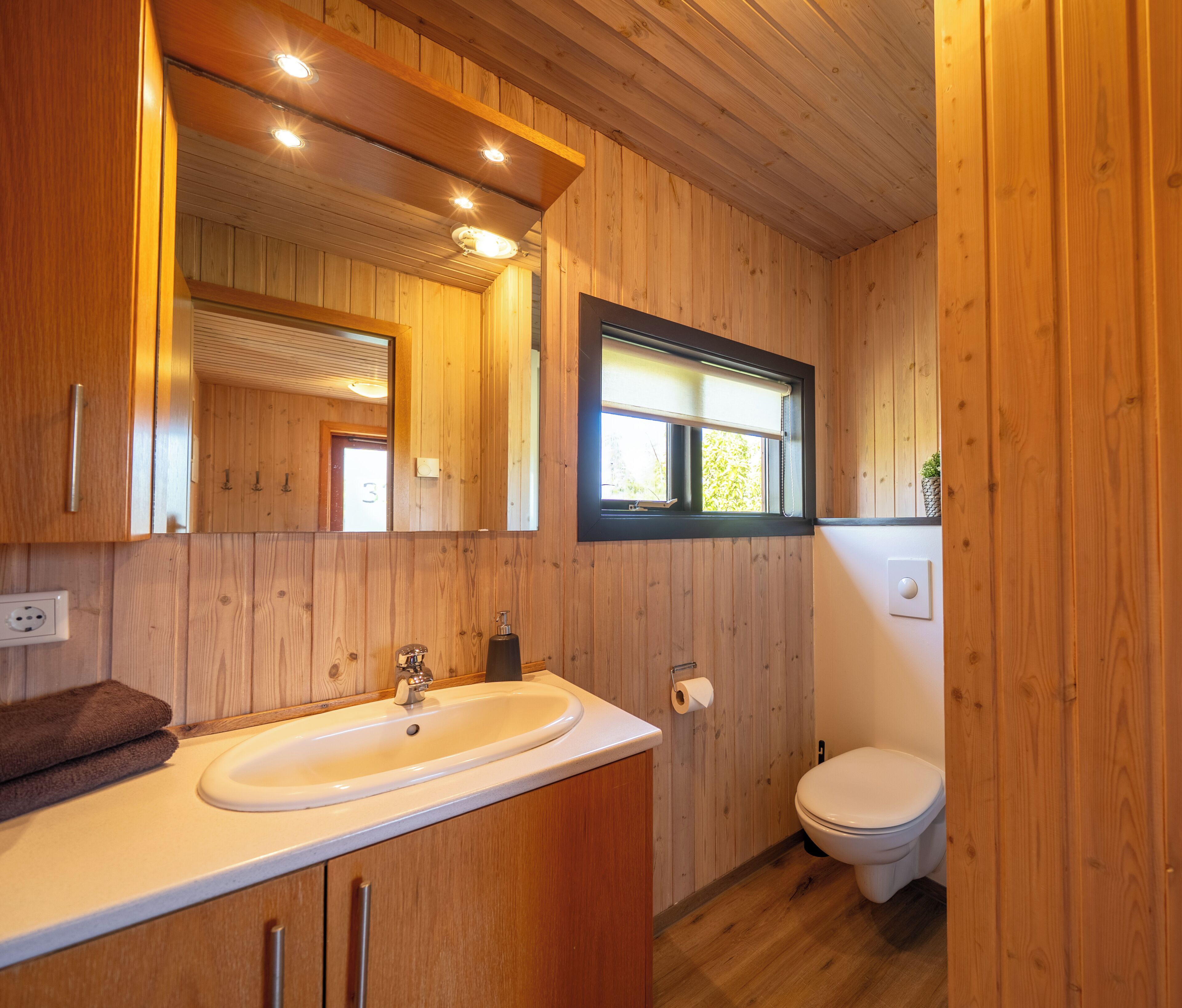 Un baño con paneles de madera, un lavabo, un espejo y un inodoro.