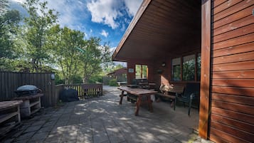 A wooden cabin with a patio, outdoor seating, and a barbecue grill.