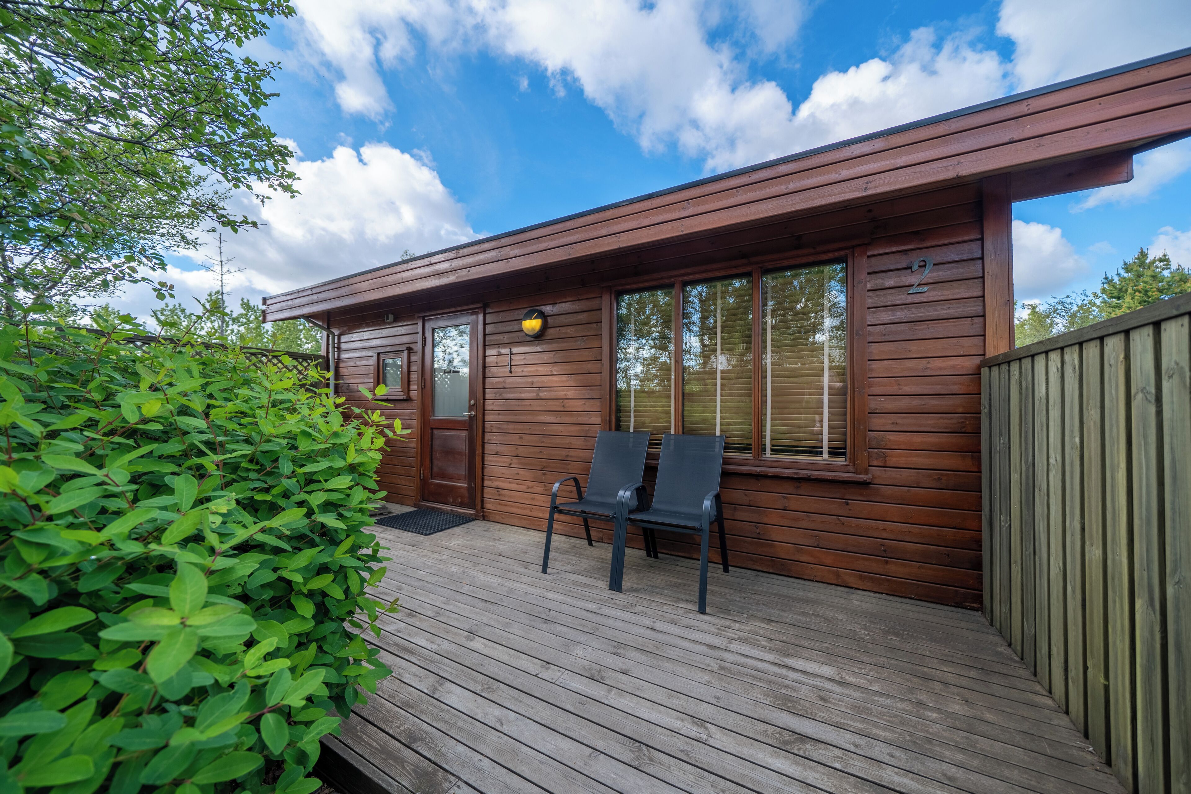 A wooden cabin with a deck, two chairs, and a door marked with the number 2.