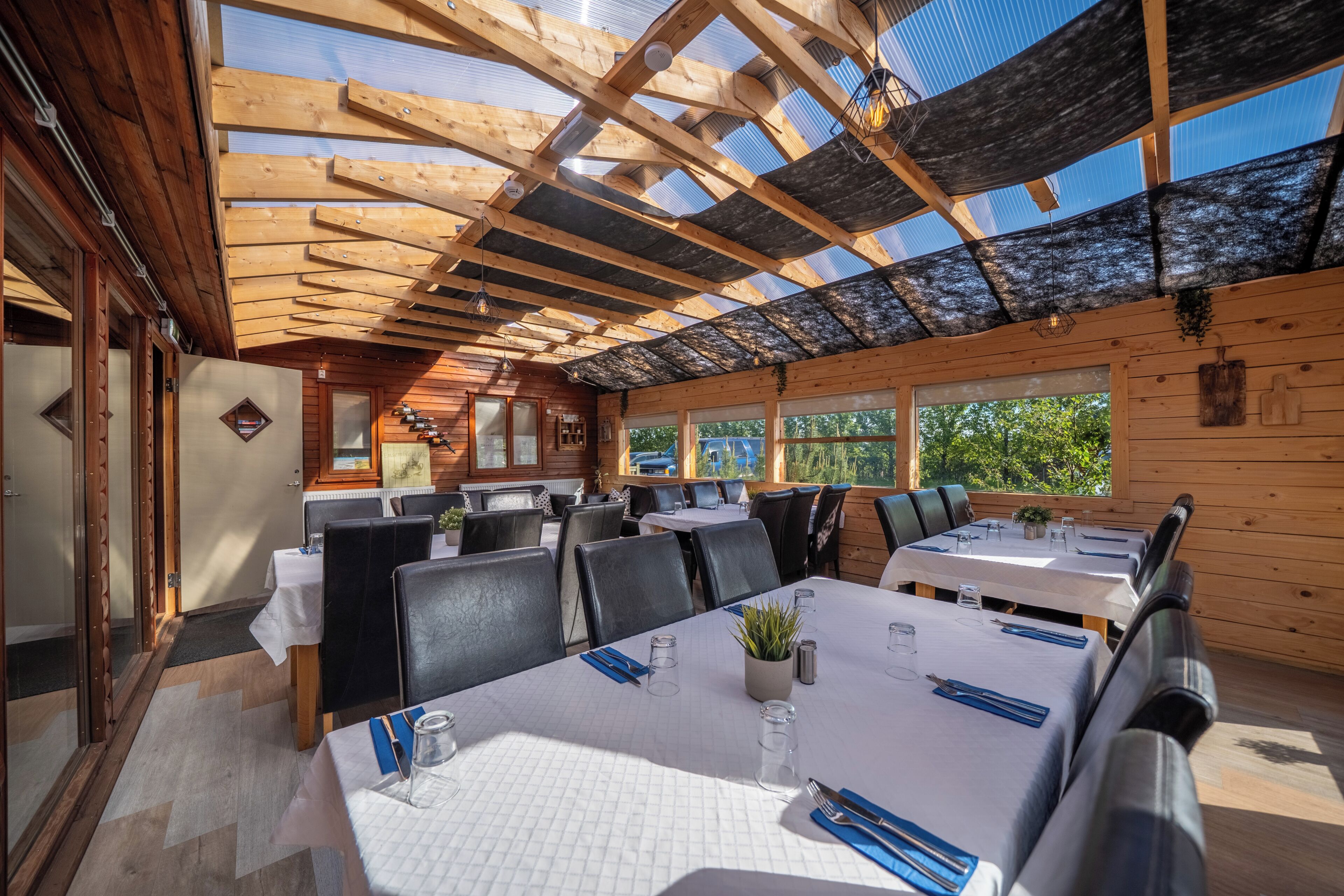 A restaurant with wooden interior, tables set with white tablecloths, and a glass ceiling.