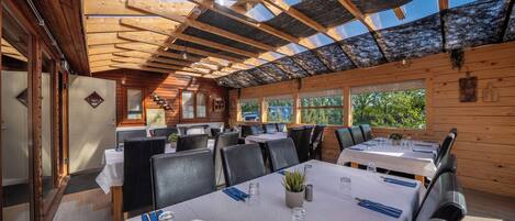 Un restaurante con interior de madera, mesas dispuestas con manteles blancos y un techo de vidrio.