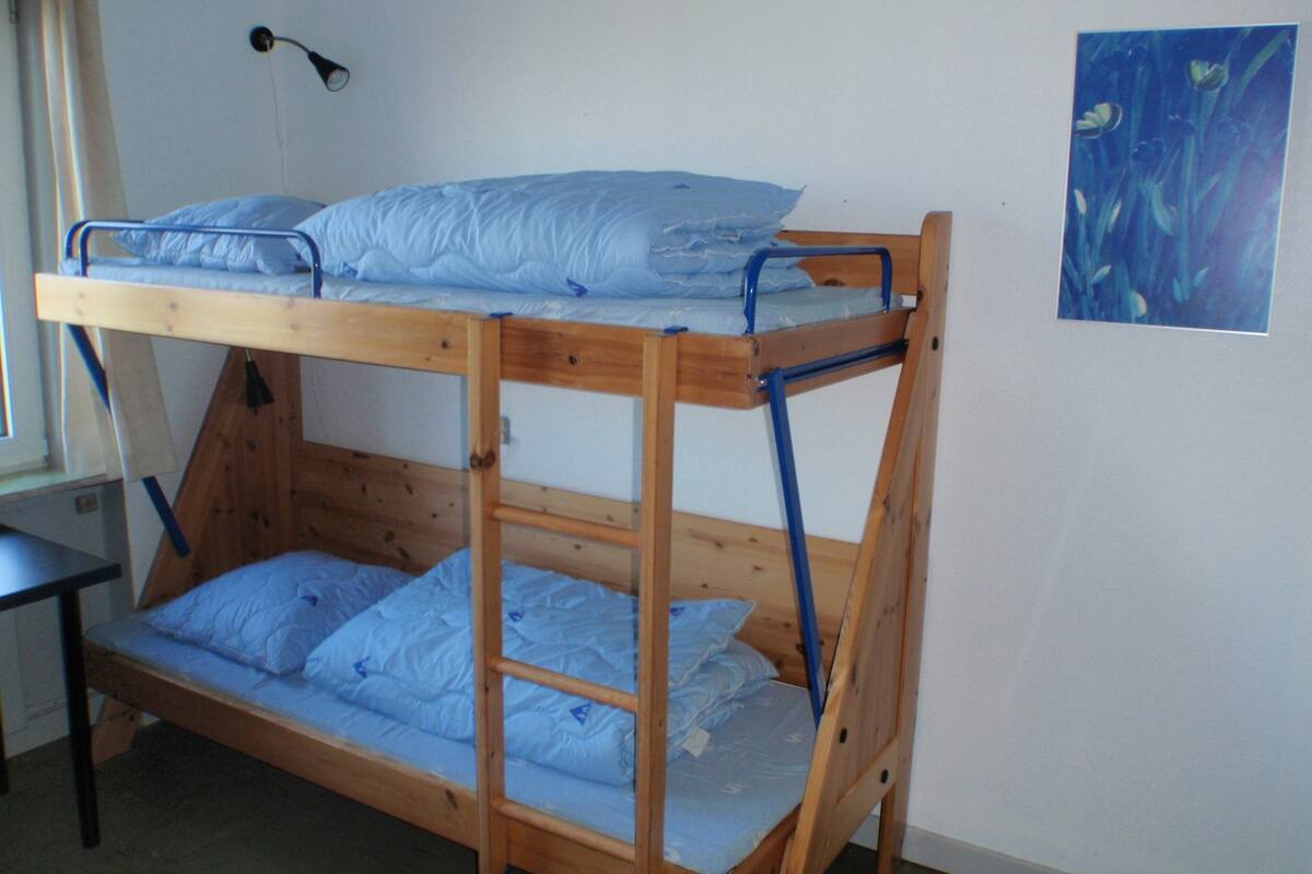 A bunk bed with two levels, a bedside table, and a wall-mounted lamp.