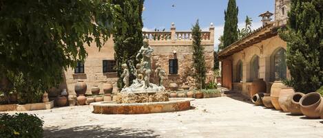 A courtyard with a fountain, terracotta pots, and a building with arches and a balcony.
