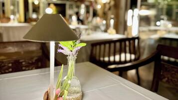 A table with a glass vase containing flowers and a candle, set on a white tablecloth.