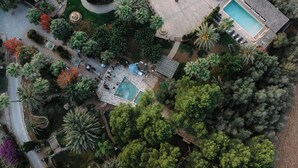 Vue aérienne d’un complexe hôtelier doté d’une piscine, de jardins aménagés et d’une fontaine circulaire.