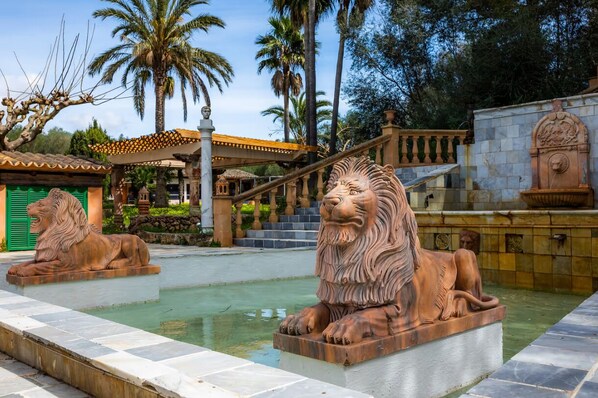 A courtyard with two lion statues, a fountain, and a building with a tiled roof.