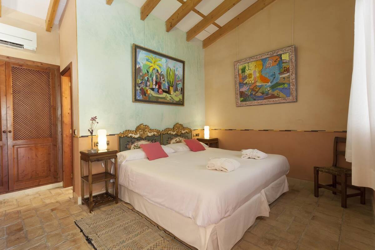 Een hotelkamer met een groot bed, twee nachtkastjes, een houten garderobe en twee schilderijen aan de muur.