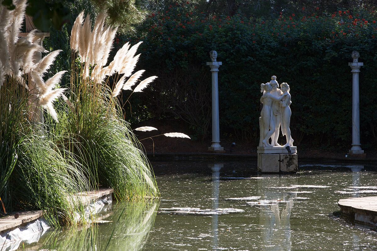 A statue in a garden with a pond, surrounded by greenery and a stone balustrade.