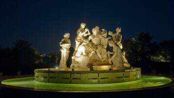 A nighttime sculpture fountain with multiple figures, surrounded by a circular pool with a greenish hue.