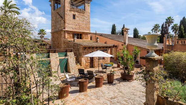 Un bâtiment en pierre doté d’une tour, un espace extérieur aménagé avec des parasols et des plantes en pot.