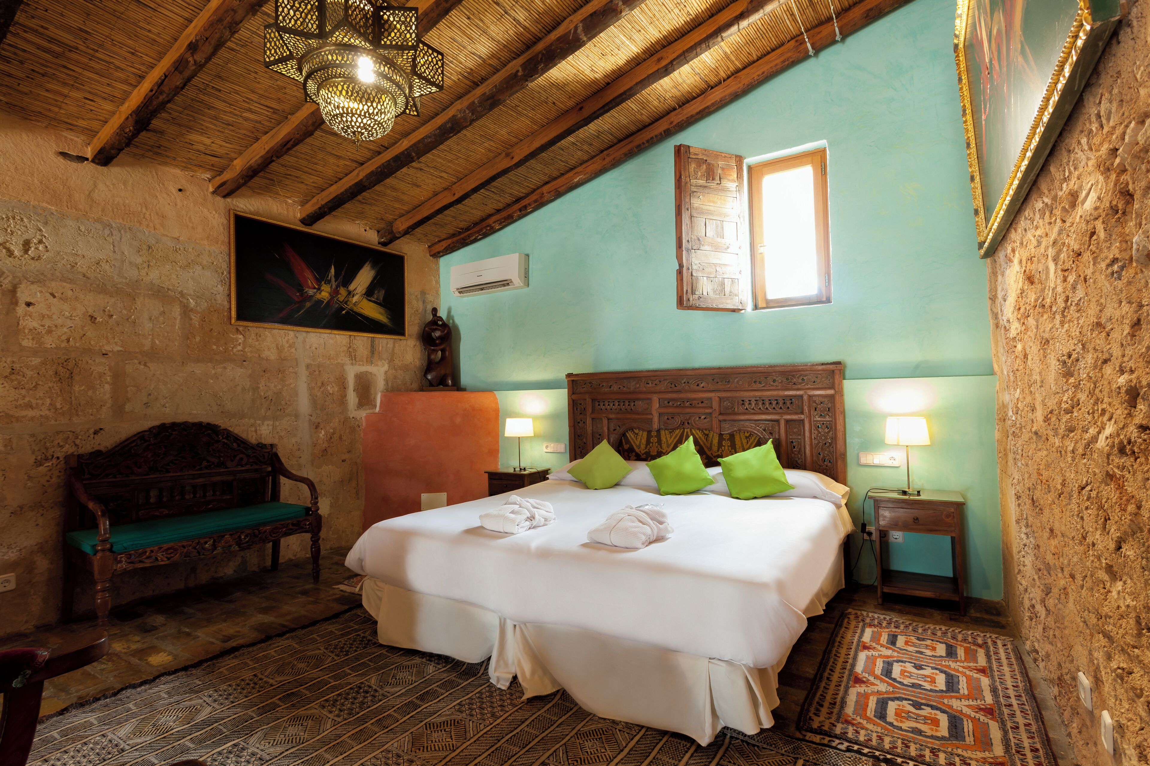 Una habitación acogedora con una cama de madera, almohadas verdes, un banco y una alfombra estampada.